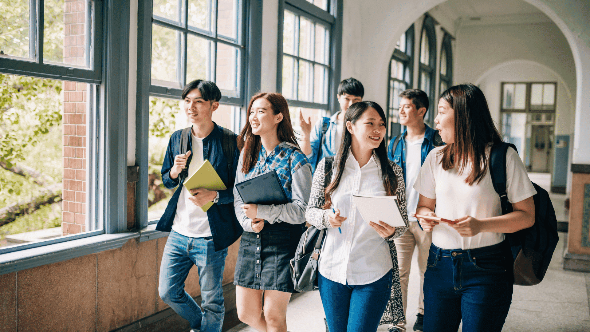 Students walking together in a bright hallway, carrying books and talking.